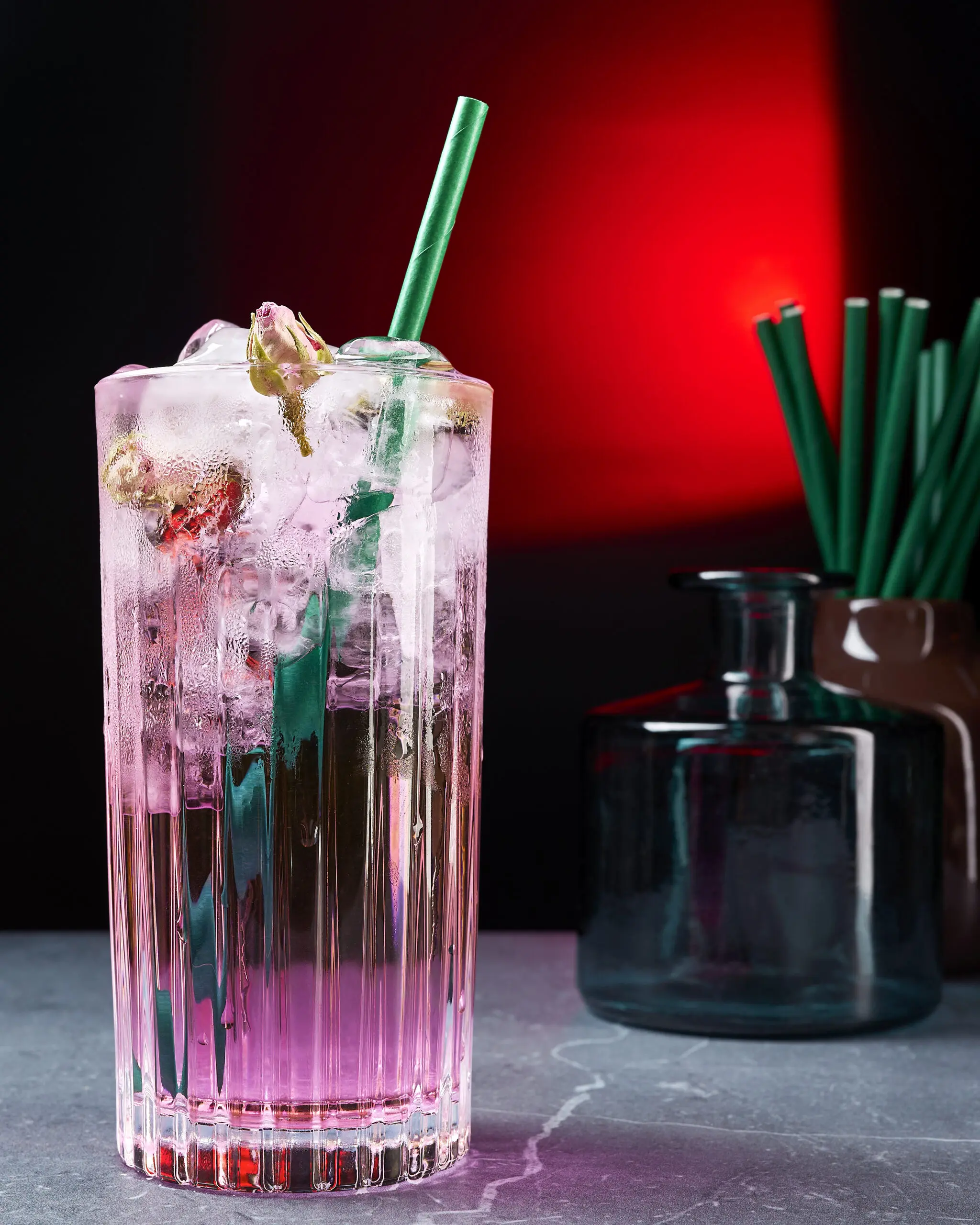 Cocktail rosa con ghiaccio e petali di rosa in bicchiere alto