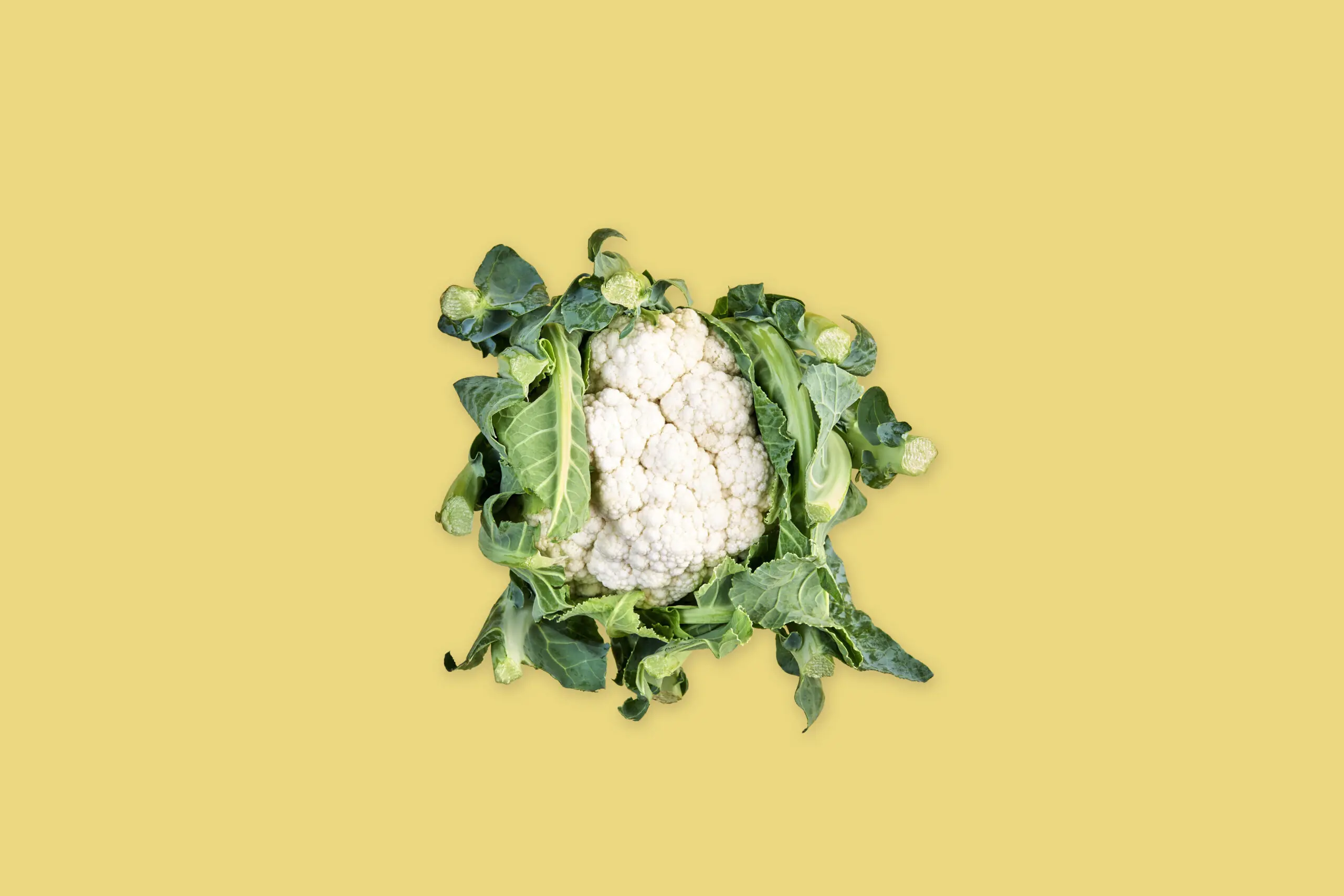 Cavolfiore intero con foglie verdi su sfondo giallo, fotografia di prodotto food