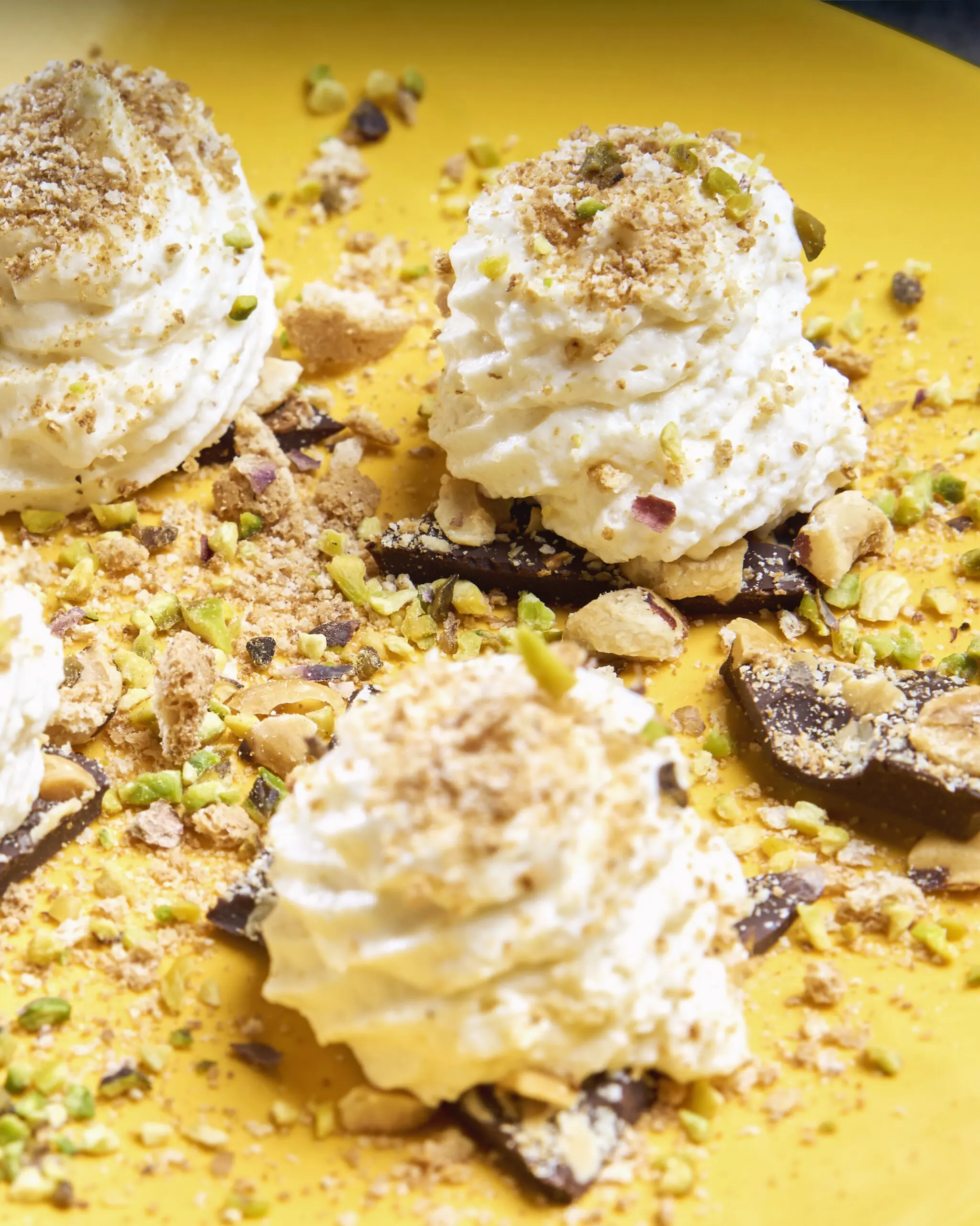 Primo piano di dessert con crema e granella di pistacchio su piatto giallo