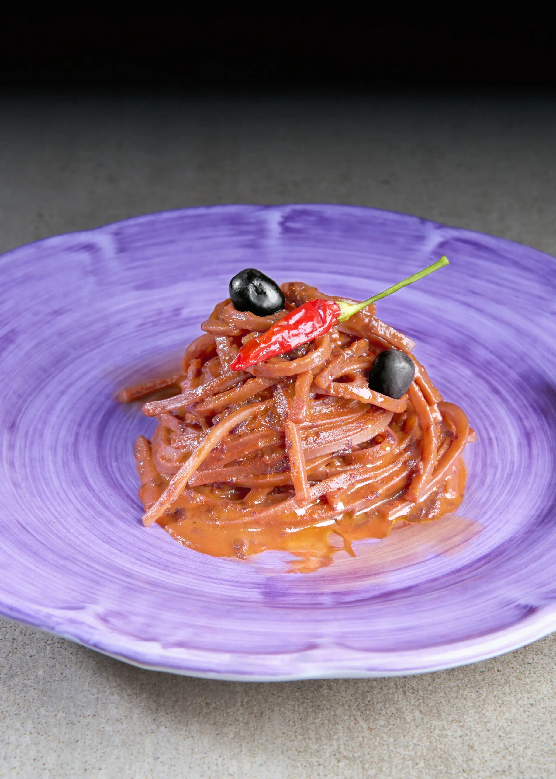 Piatto di pasta al pomodoro con olive e guarnizione su piatto viola