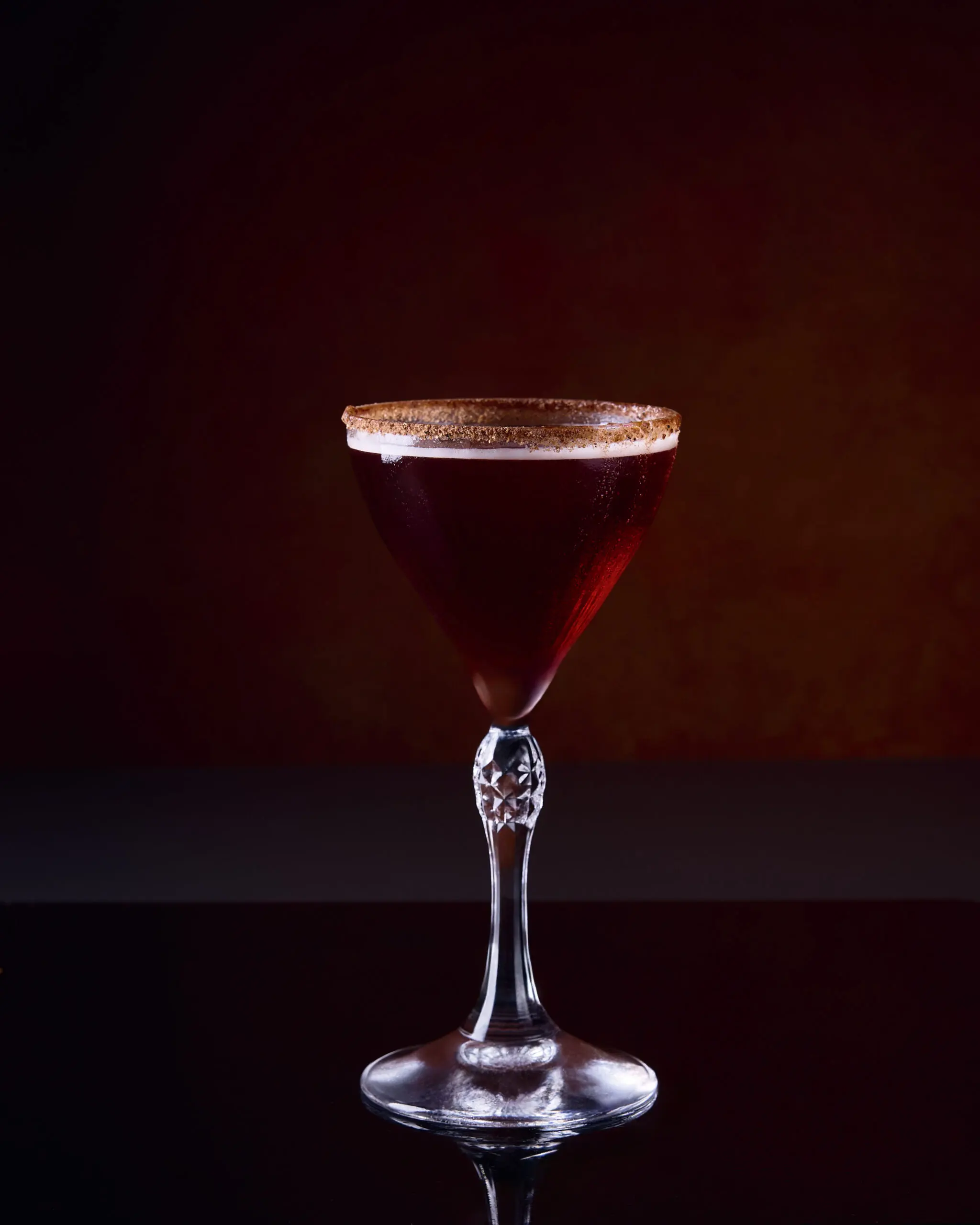 Cocktail rosso in coppa martini su sfondo scuro con luce da studio