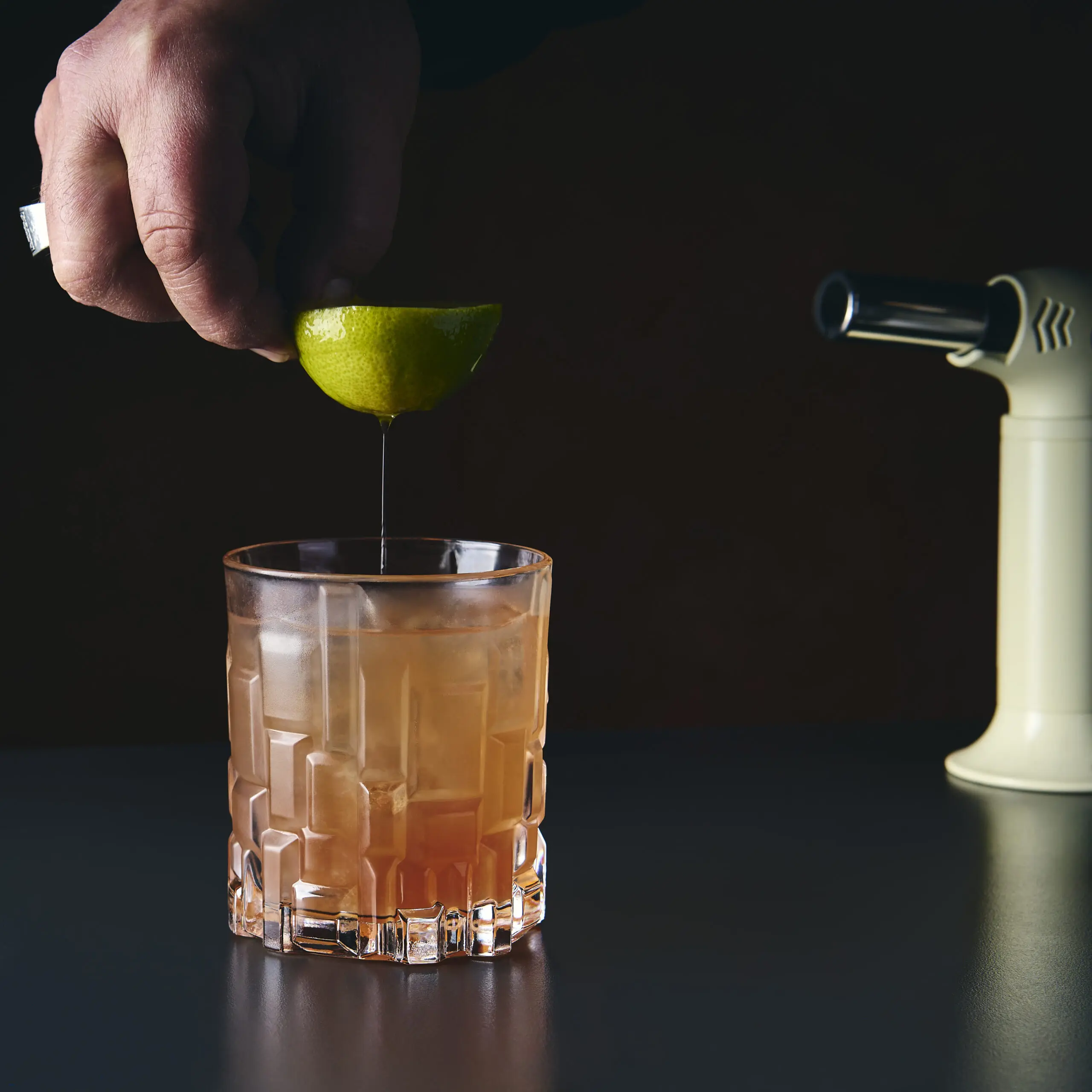 Mano che aggiunge lime a un cocktail in bicchiere basso durante la preparazione al bar