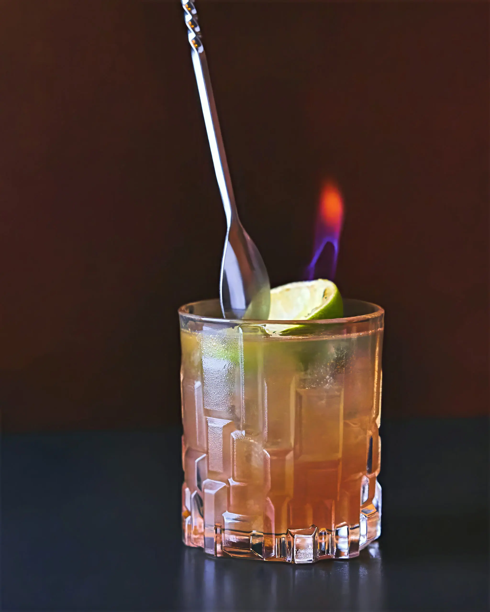 Cocktail in bicchiere basso con lime e fiamma blu durante la preparazione