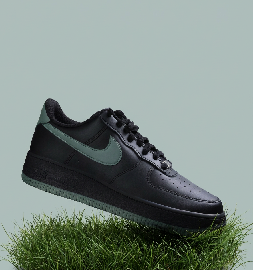 Sneaker nera con logo verde salvia sospesa sopra un ciuffo d’erba su sfondo verde chiaro.